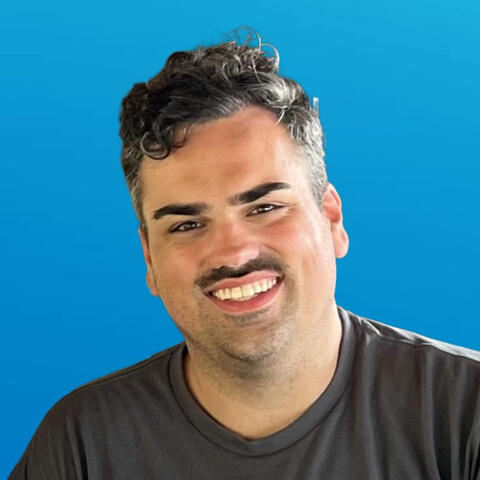 headshot of John Kliewer smiling against a blue background wearing a dark grey t-shirt